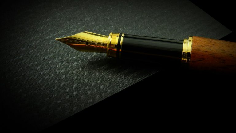 Detailed close-up of a classic fountain pen nib on textured black paper, showcasing elegance.