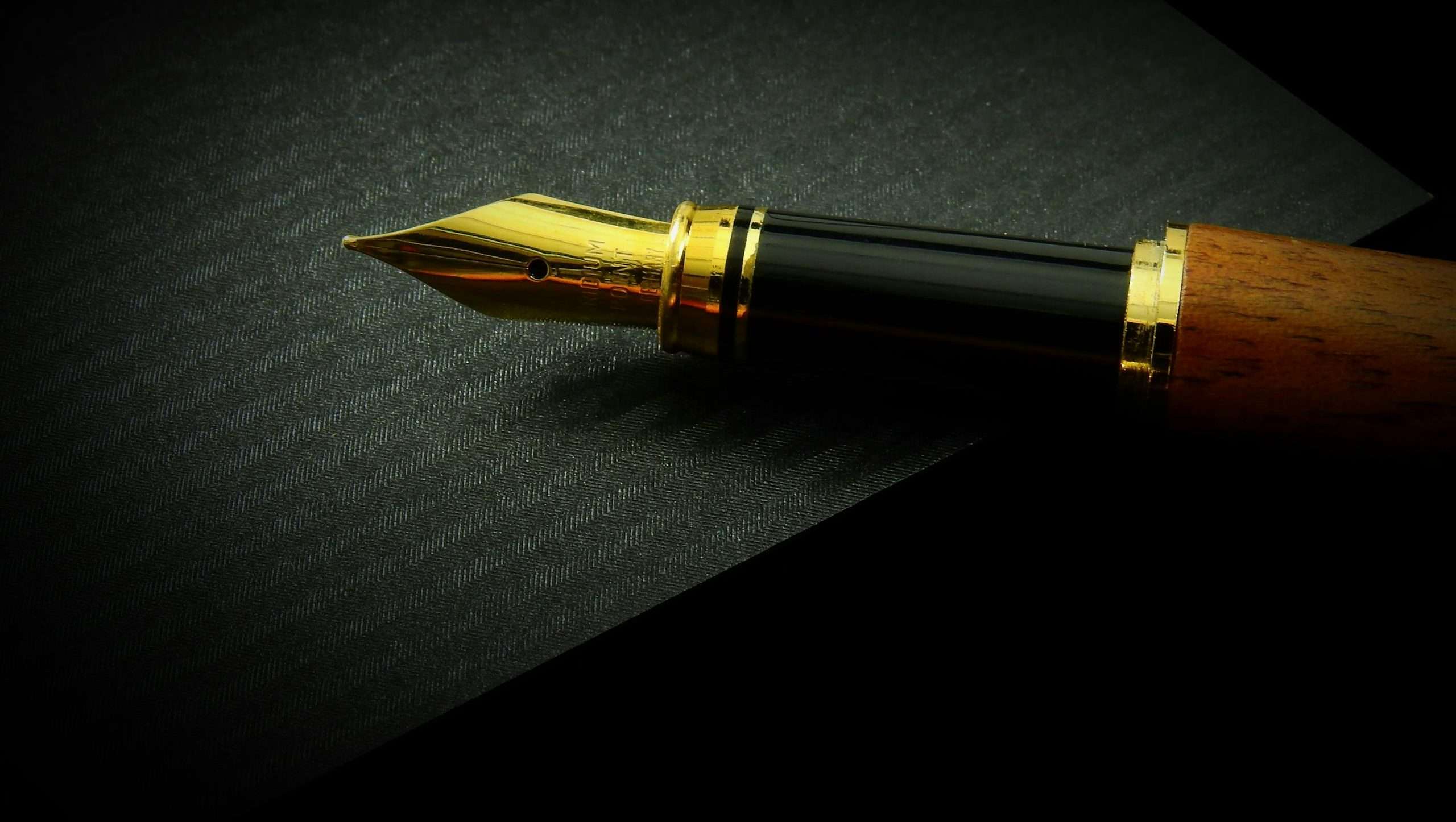 Detailed close-up of a classic fountain pen nib on textured black paper, showcasing elegance.