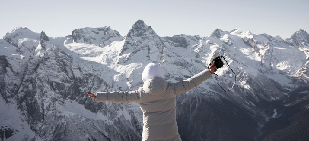 Person enjoying a snowy mountain view, capturing the moment with a camera.