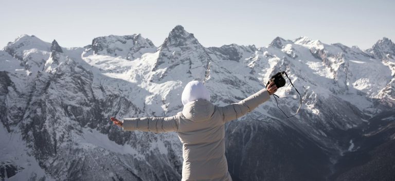 Person enjoying a snowy mountain view, capturing the moment with a camera.