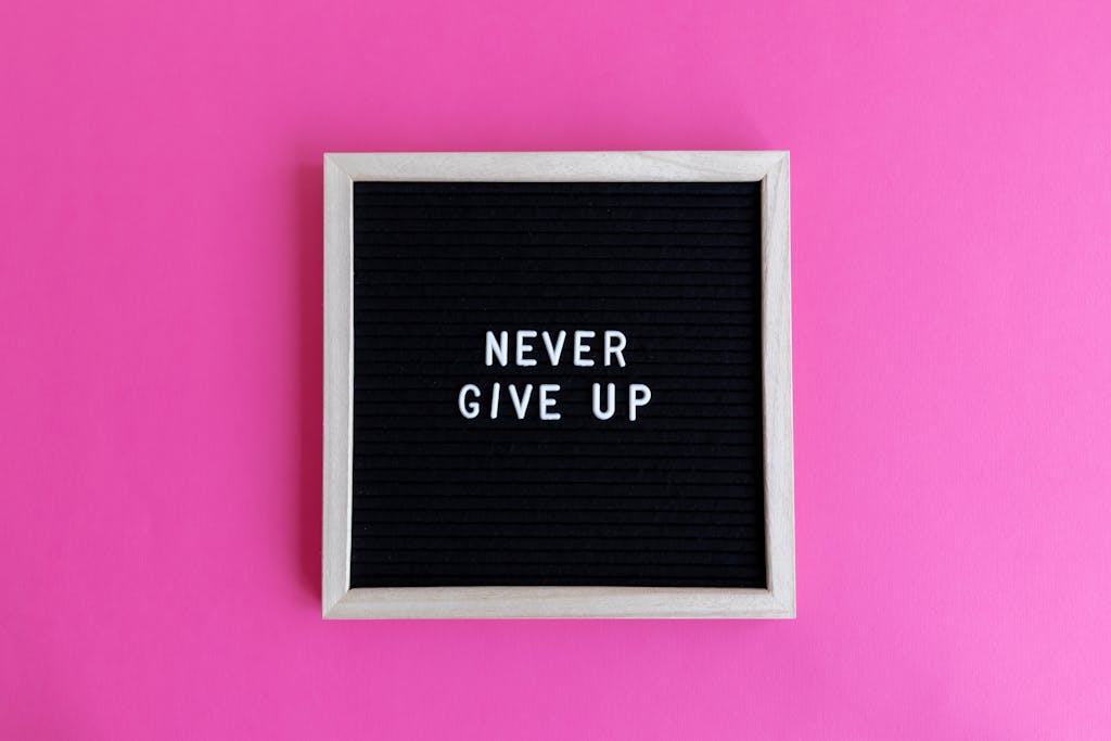 A framed letter board with 'NEVER GIVE UP' on a vibrant pink background.