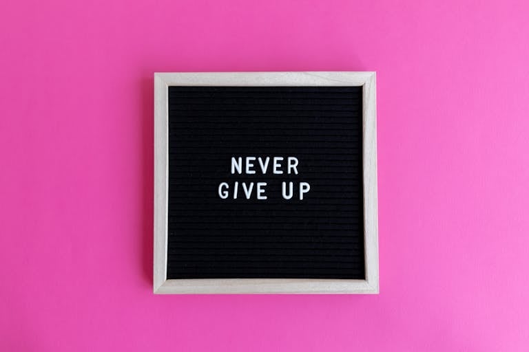 A framed letter board with 'NEVER GIVE UP' on a vibrant pink background.
