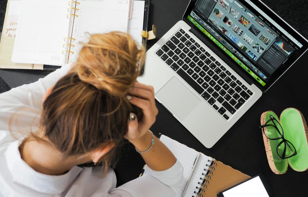 Overhead view of a stressed woman working at a desk with a laptop, phone, and notebooks.